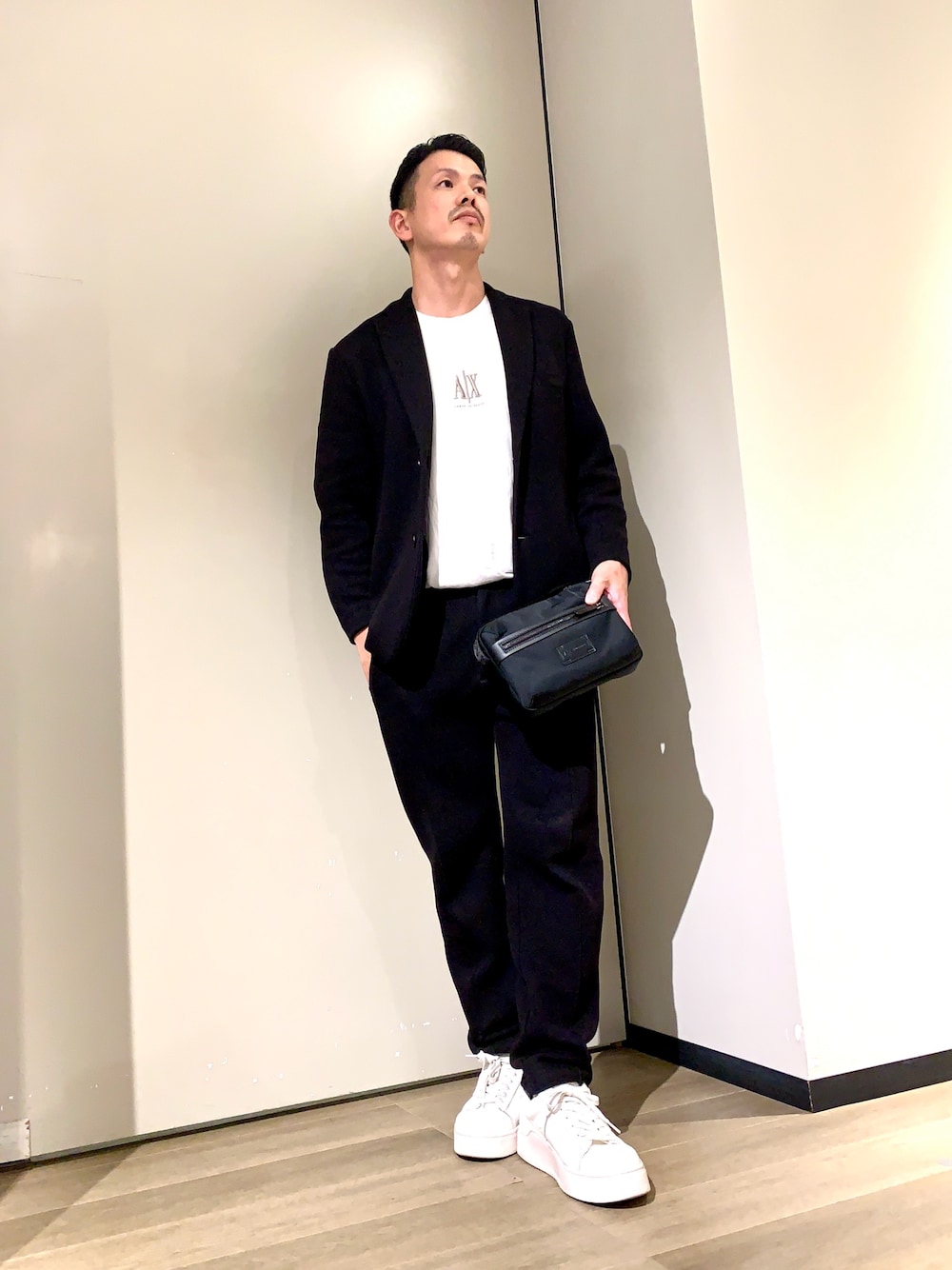ホワイト系のスニーカー、ブラック系のスラックス、ブラック系のショルダーバッグを着用したメンズの秋コーディネートの1枚目の写真