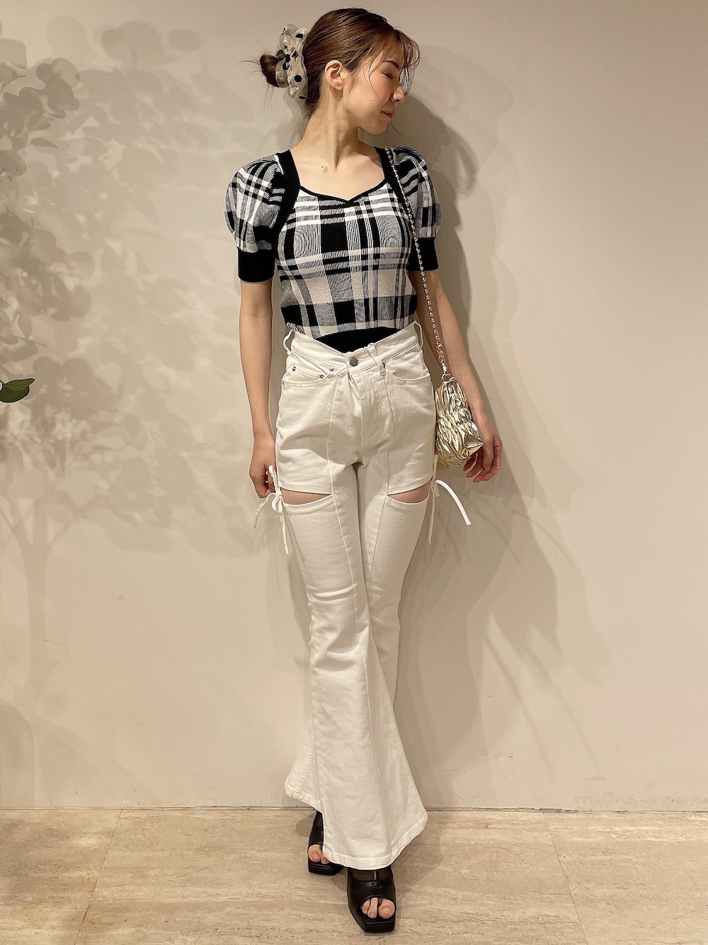 ブラック系のニット/セーター、ホワイト系のデニムパンツ、ゴールド系のハンドバッグを着用したレディースの春コーディネートの1枚目の写真