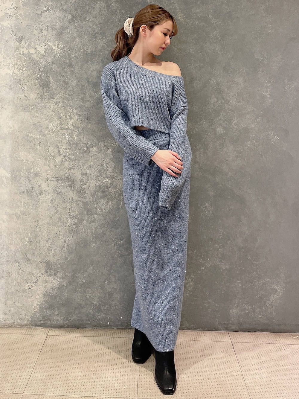 ブルー系のニット/セーター、ブルー系のスカート、ブラック系のブーツを着用したレディースの秋コーディネートの1枚目の写真