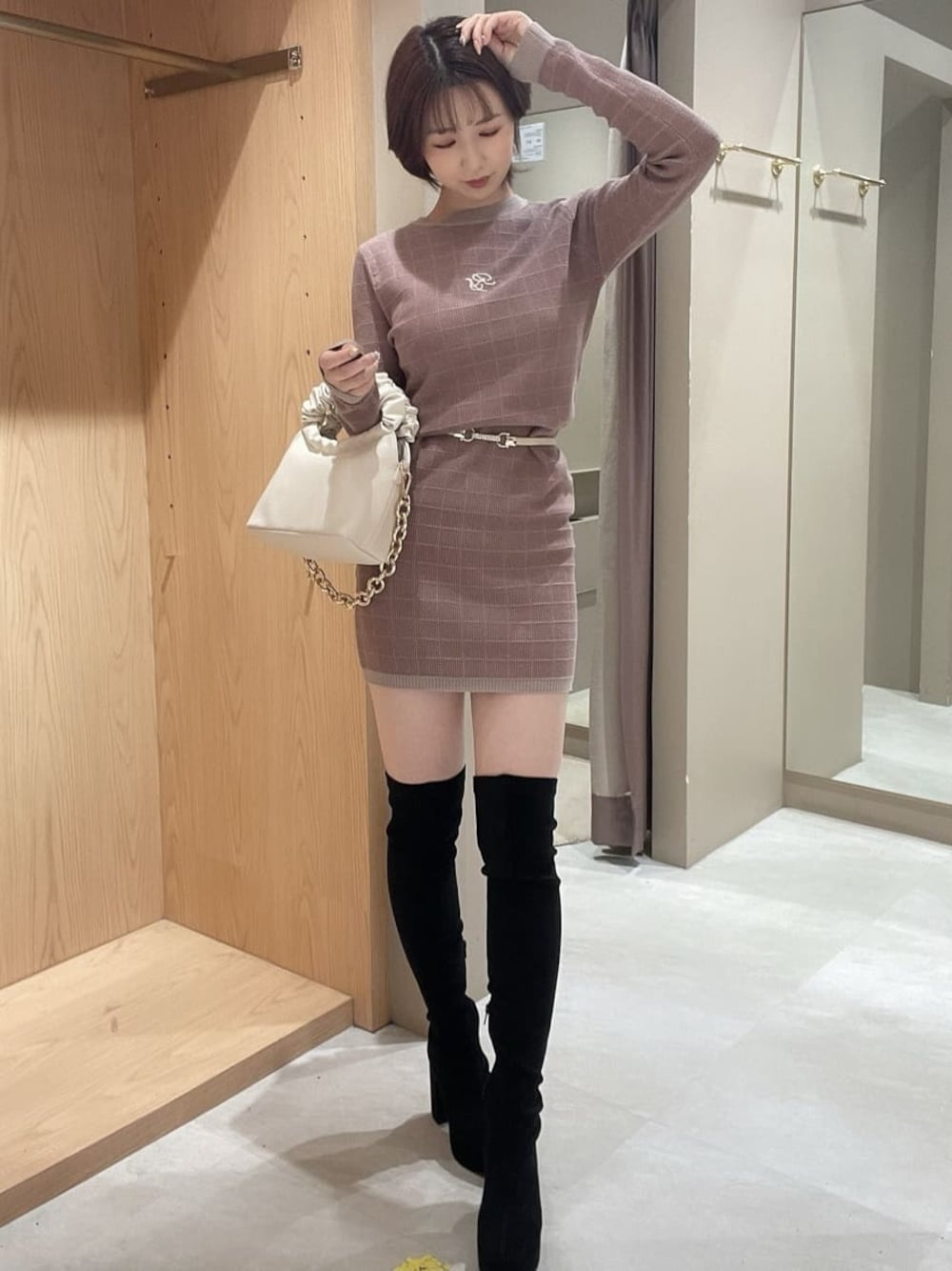 ブラック系のブーツ、ベージュ系のワンピース、ホワイト系のハンドバッグを着用したレディースの秋コーディネートの1枚目の写真