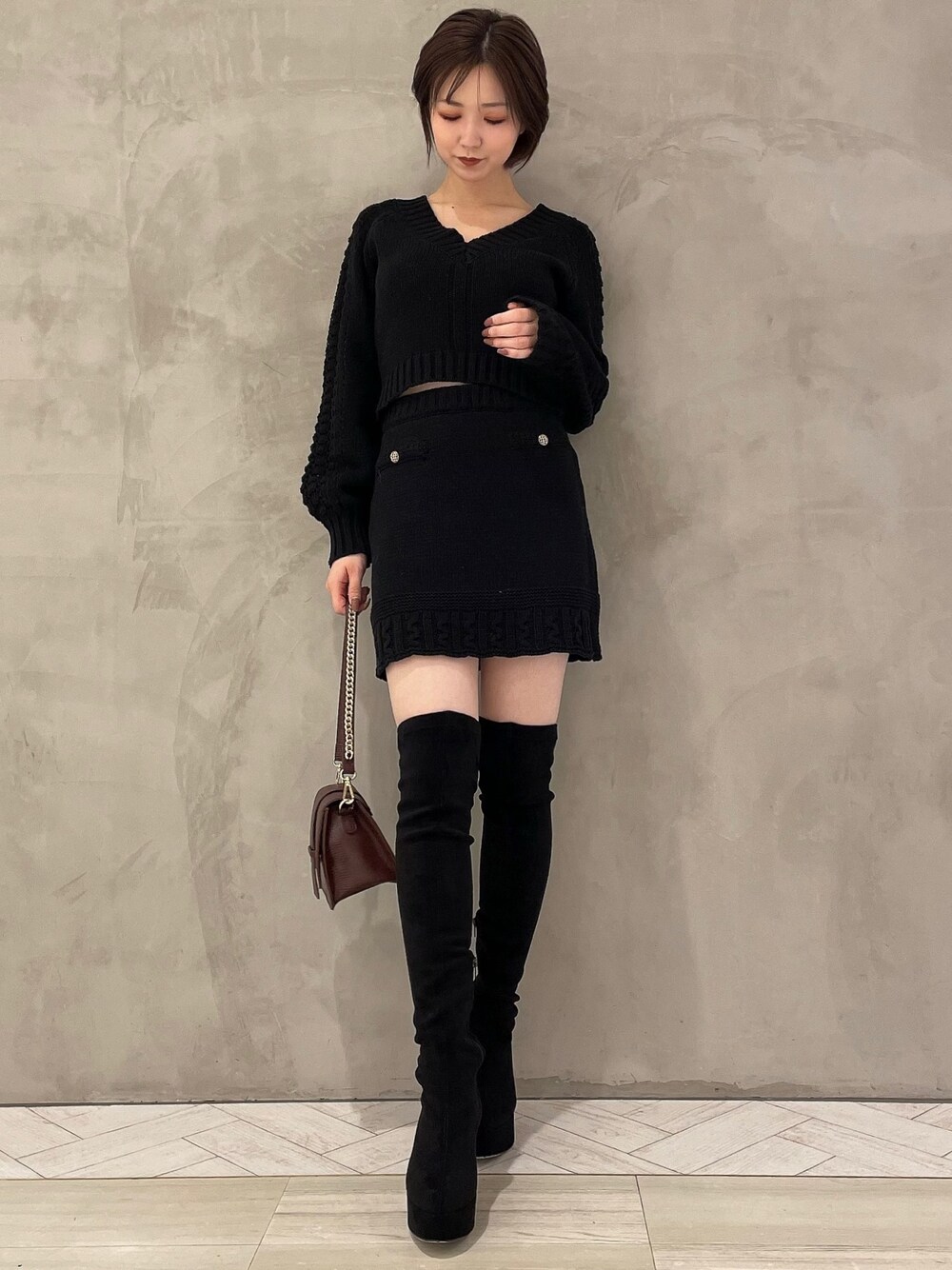 ブラウン系のハンドバッグ、ブラック系のブーツ、ブラック系のニット/セーターを着用したレディースの秋コーディネートの1枚目の写真