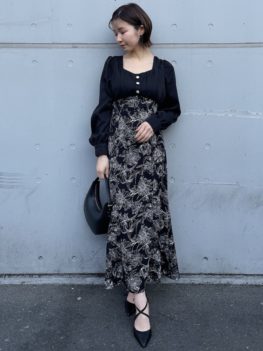 ベージュ系のトレンチコート、ブラック系のワンピース、ブラック系のハンドバッグを着用したレディースの冬コーディネートの1枚目の写真