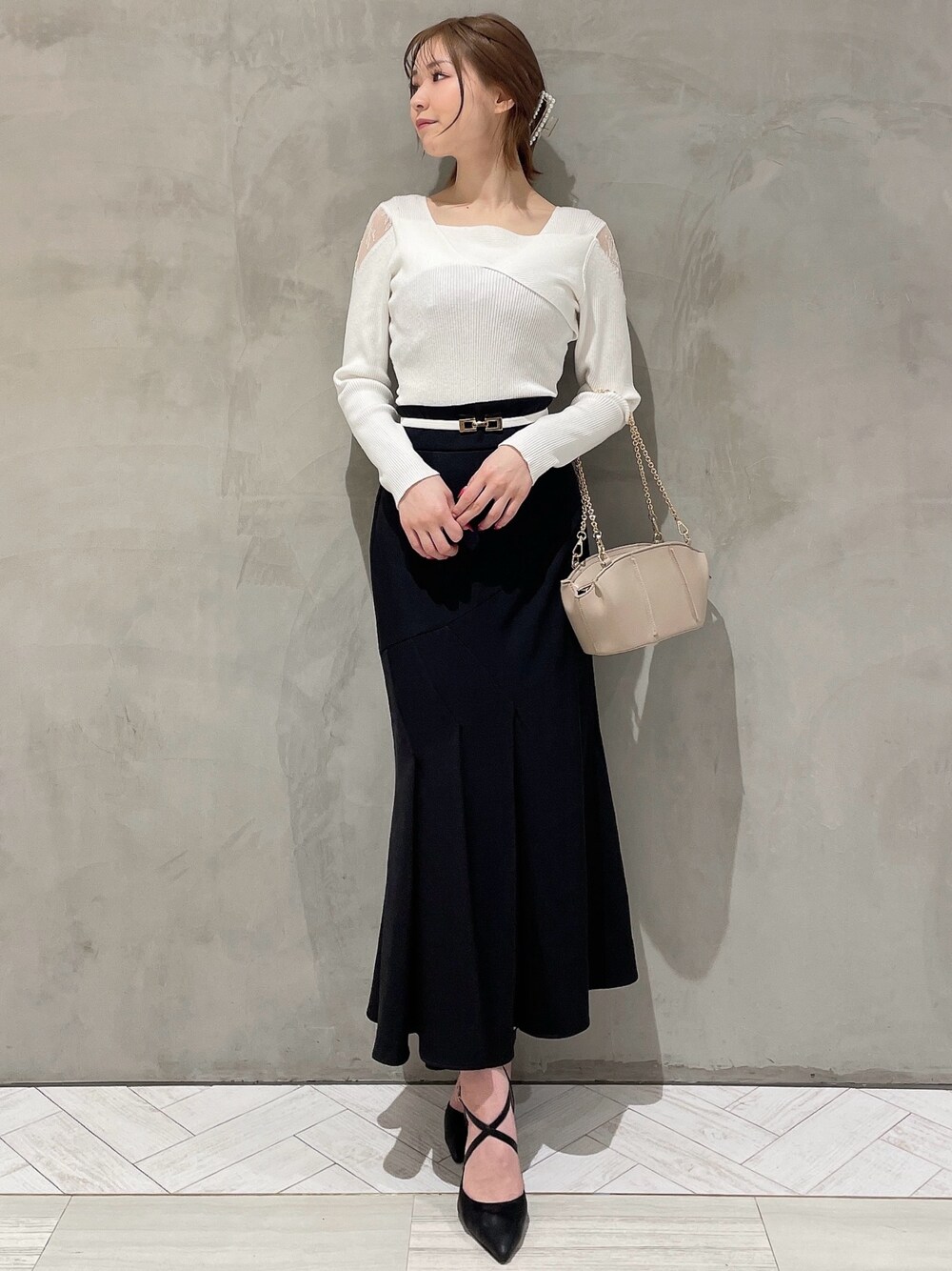 ホワイト系のニット/セーター、ベージュ系のハンドバッグ、ブラック系のスカートを着用したレディースの冬コーディネートの1枚目の写真