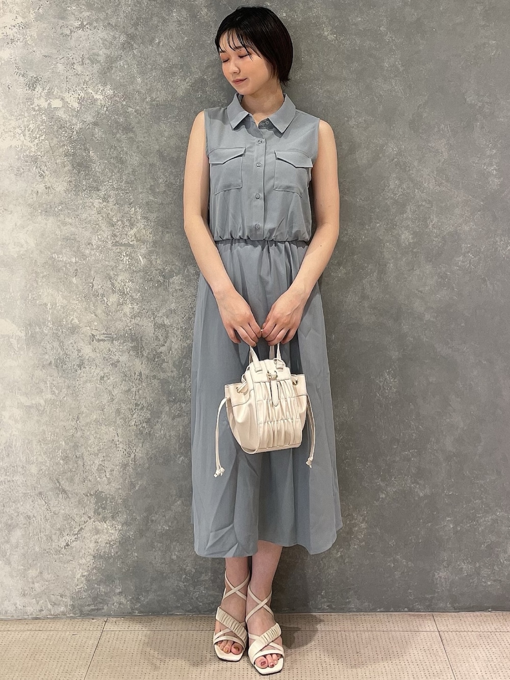 ホワイト系のハンドバッグ、ホワイト系のサンダル、ブルー系のシャツワンピースを着用したレディースの夏コーディネートの1枚目の写真