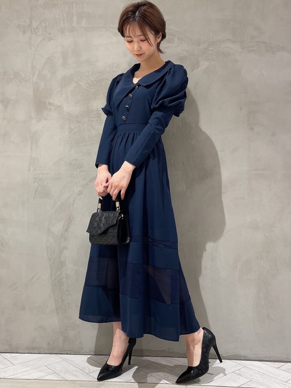 ブラック系のハンドバッグ、ブルー系のワンピース、ブラック系のパンプスを着用したレディースの冬コーディネートの1枚目の写真
