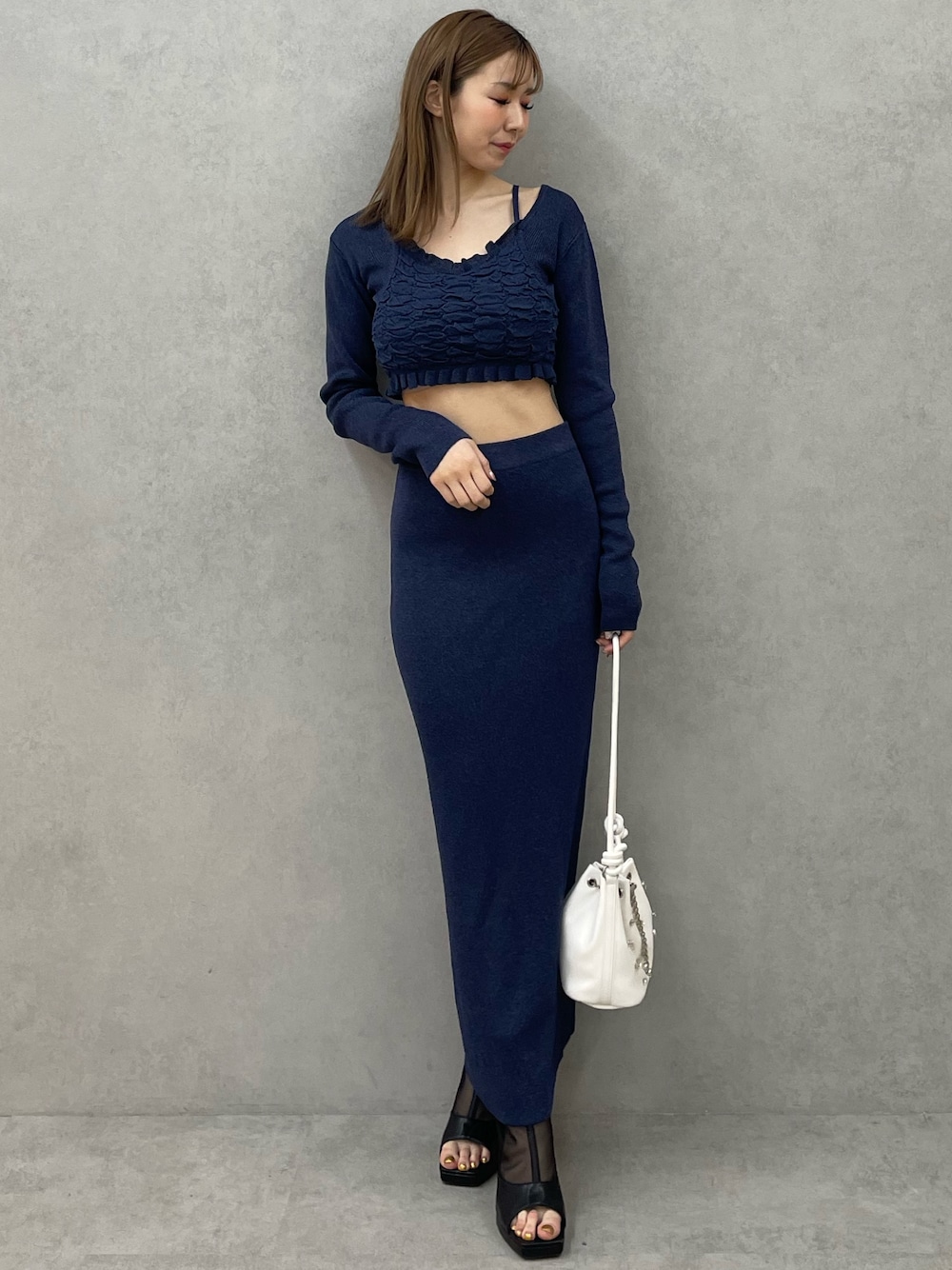 ブルー系のニット/セーター、ブルー系のスカート、ホワイト系のハンドバッグを着用したレディースの春コーディネートの1枚目の写真