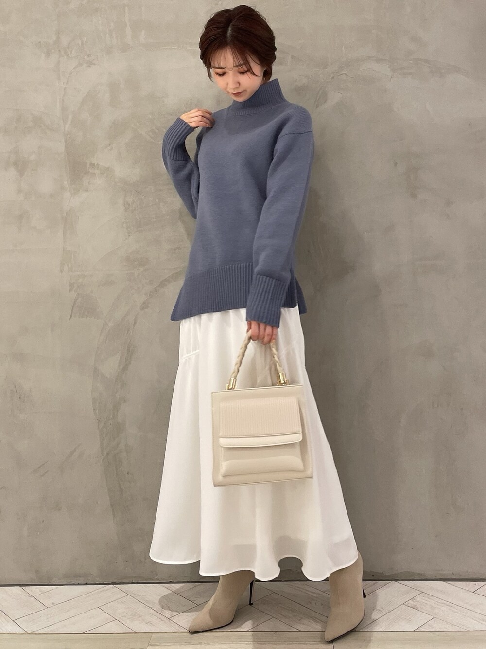 ホワイト系のブーツ、ホワイト系のハンドバッグ、ブルー系のニット/セーターを着用したレディースの冬コーディネートの1枚目の写真
