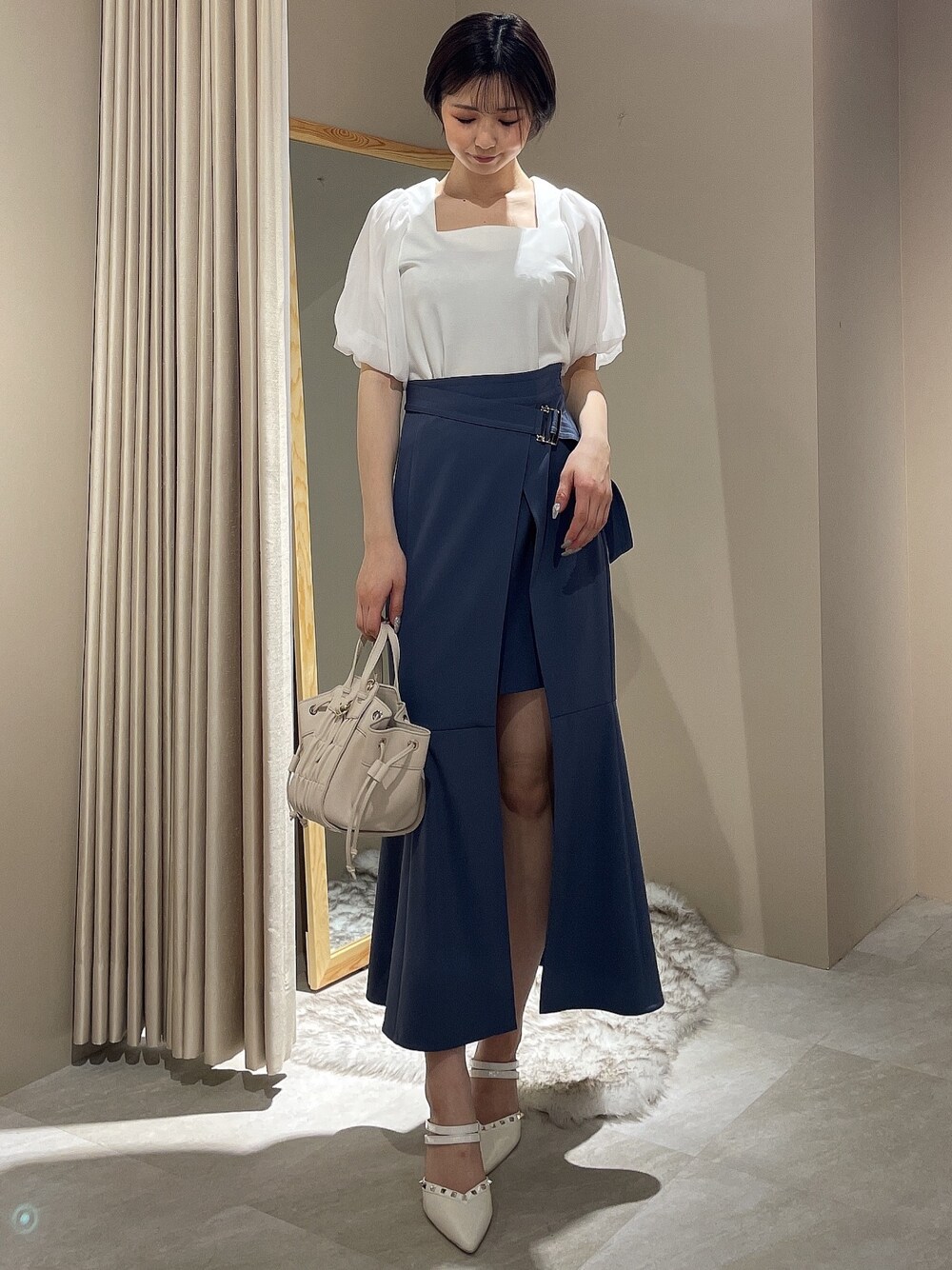 ホワイト系のハンドバッグ、ホワイト系のパンプス、ブルー系のスカートを着用したレディースの春コーディネートの1枚目の写真