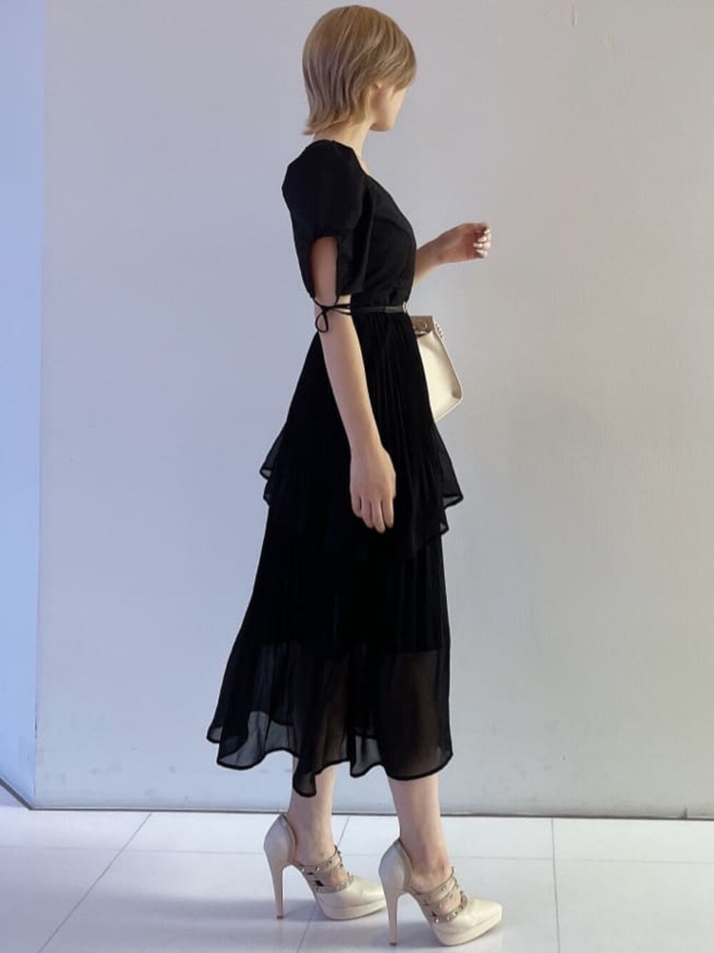 ホワイト系のハンドバッグ、ブラック系のワンピース、ベージュ系のパンプスを着用したレディースの夏コーディネートの1枚目の写真