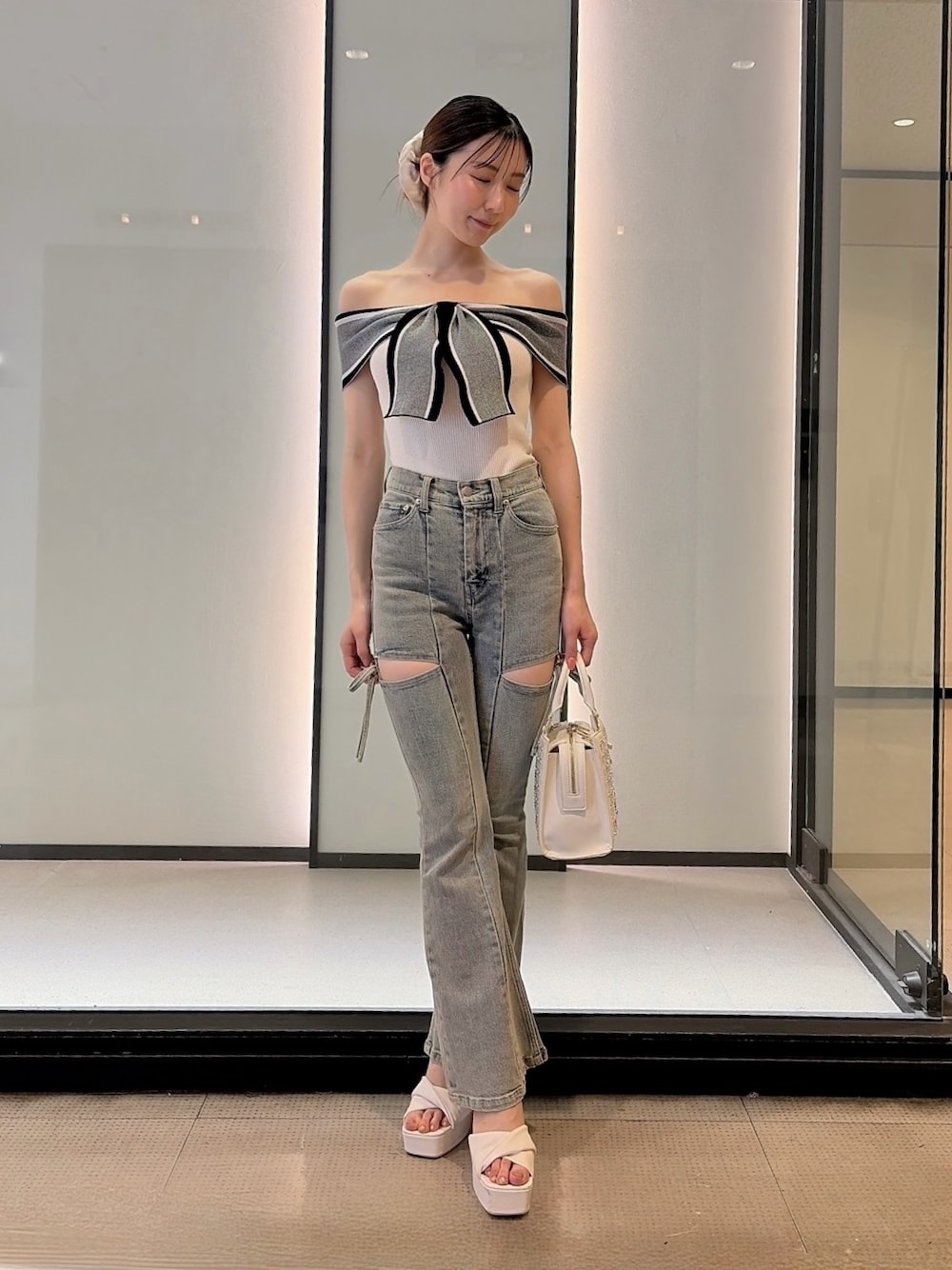 ホワイト系のニット/セーター、ブルー系のデニムパンツ、ホワイト系のハンドバッグを着用したレディースの夏コーディネートの1枚目の写真