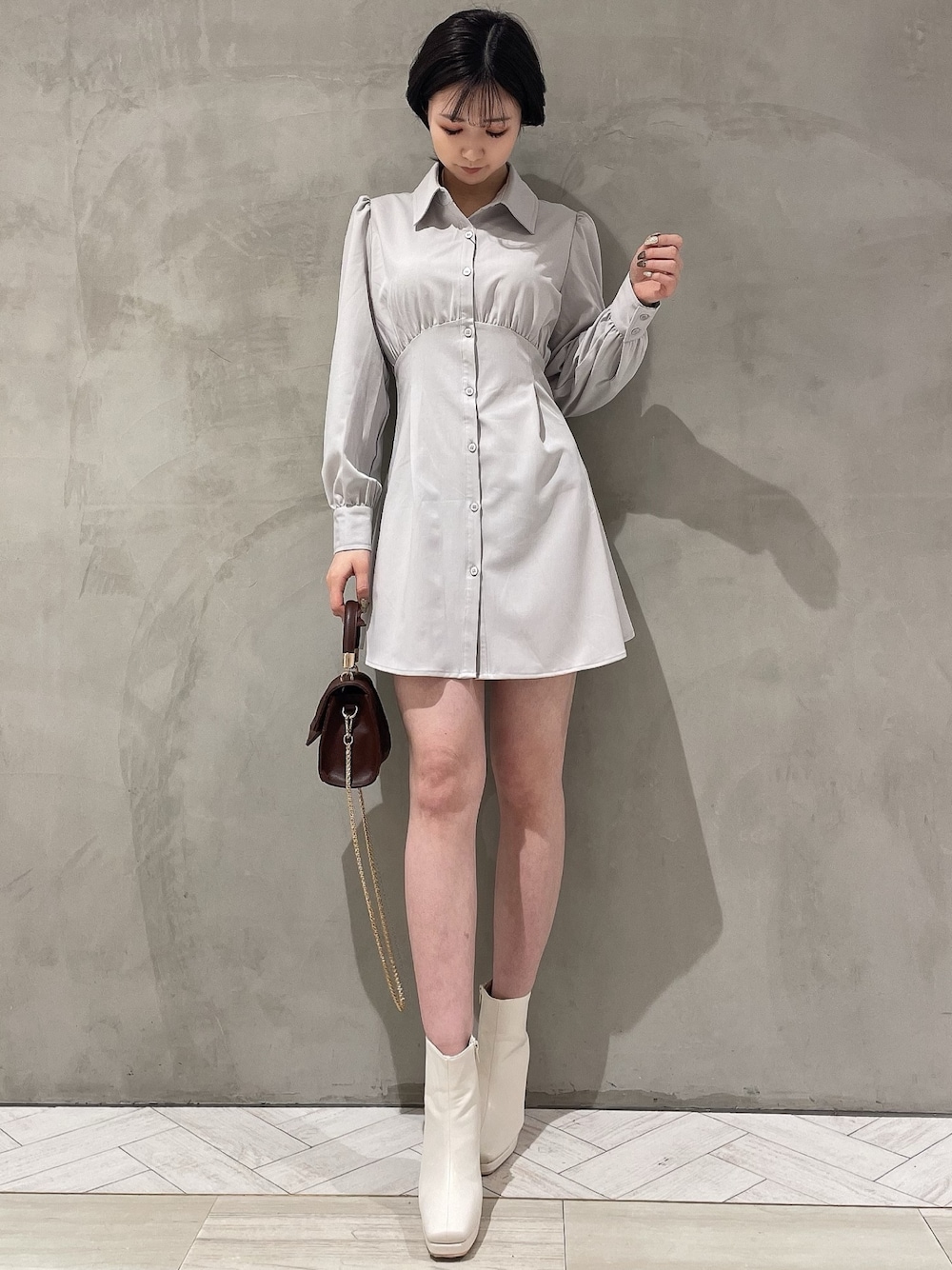 ブラウン系のハンドバッグ、ホワイト系のブーツ、グレー系のシャツワンピースを着用したレディースの冬コーディネートの1枚目の写真