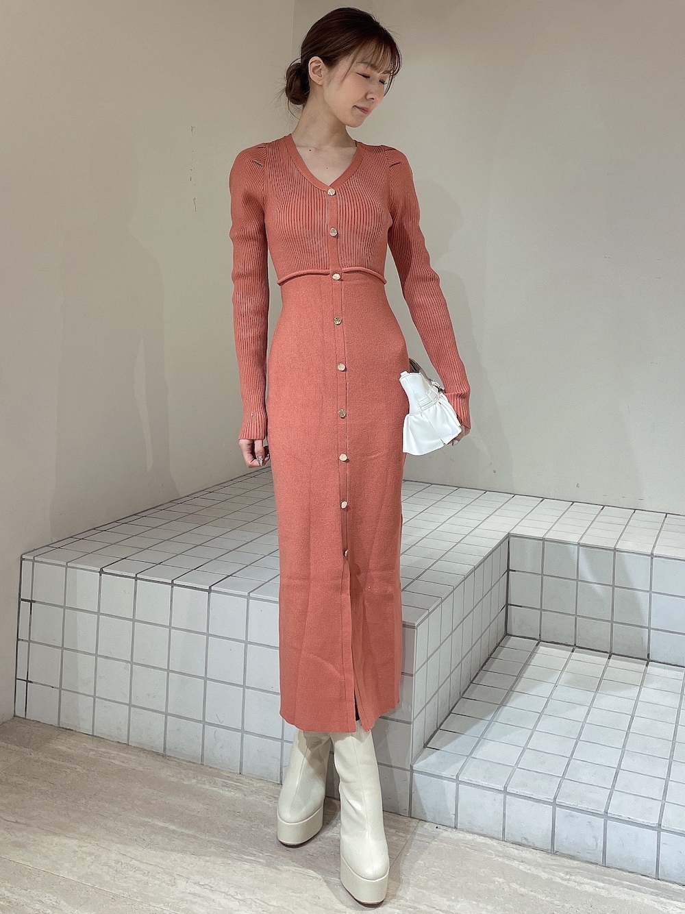 オレンジ系のワンピース、ホワイト系のハンドバッグ、ホワイト系のブーツを着用したレディースの冬コーディネートの1枚目の写真