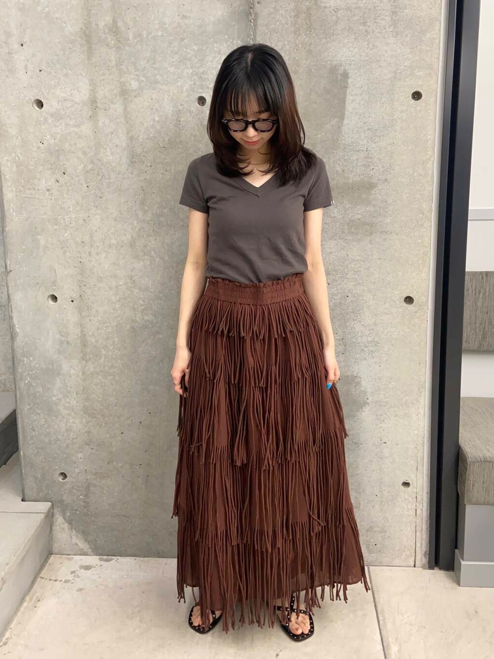 ブラウン系のスカート、ブラック系のサンダル、ブラック系のメガネを着用したレディースの春コーディネートの1枚目の写真