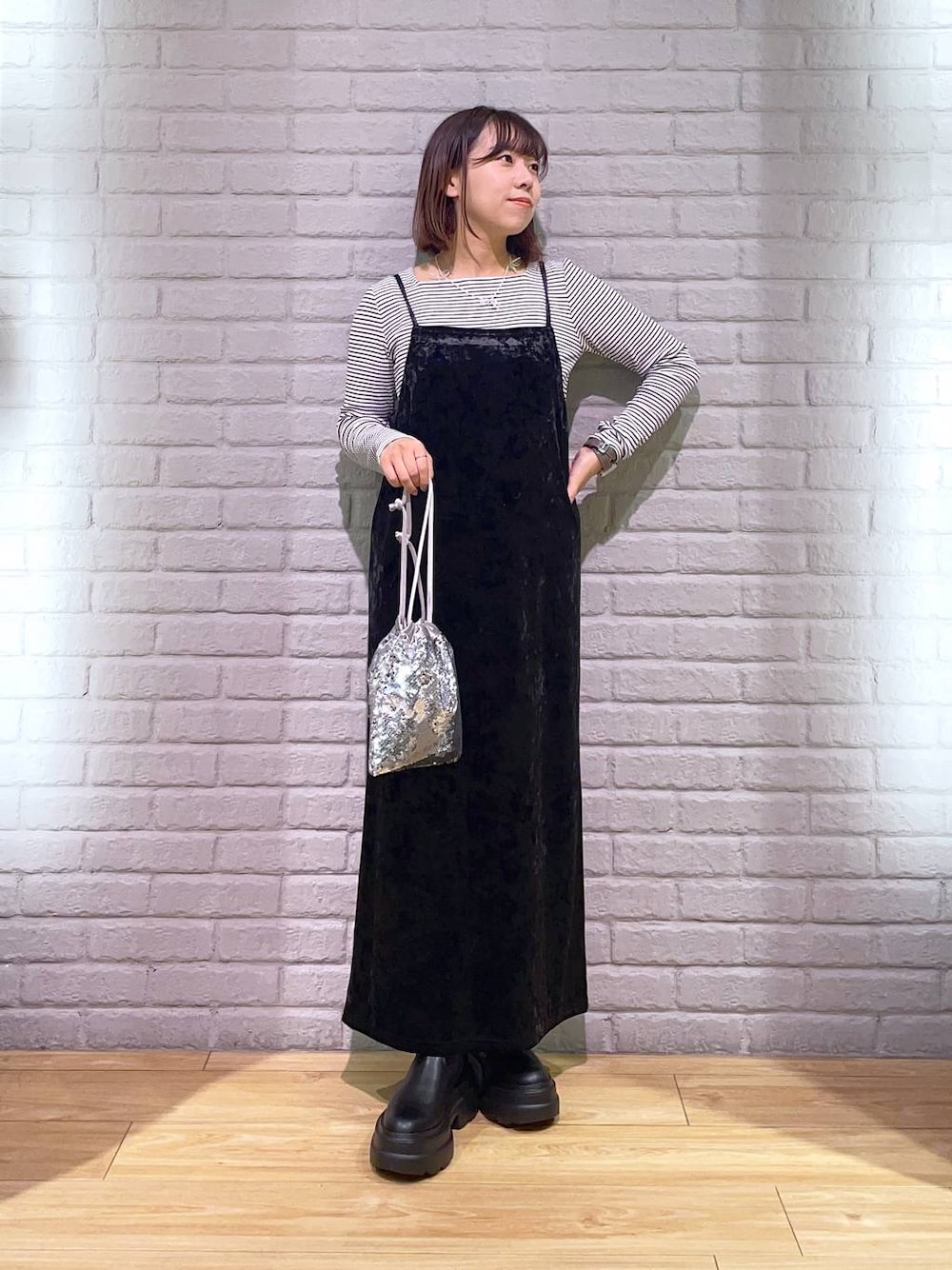 ブラック系のワンピース、ブラック系のブーツ、シルバー系のハンドバッグを着用したレディースの秋コーディネートの1枚目の写真