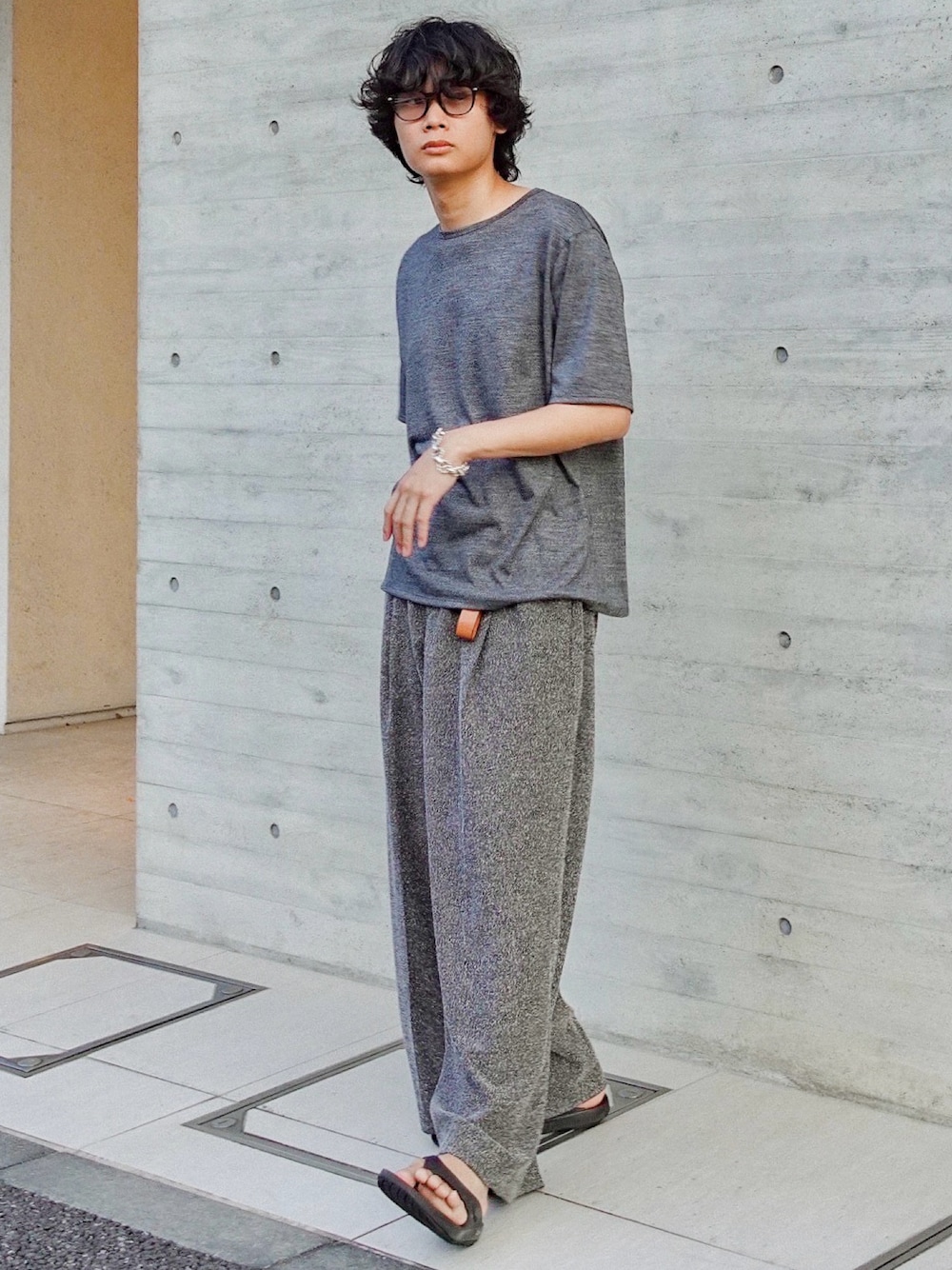 グレー系のTシャツ/カットソー、グレー系のスラックス、ブラック系のサンダルを着用したメンズの夏コーディネートの1枚目の写真