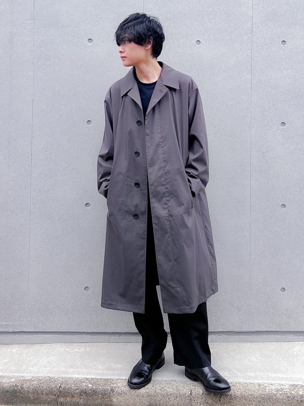 グレー系のステンカラーコート、ブラック系のスラックス、ブラック系のブーツを着用したメンズの秋コーディネートの1枚目の写真