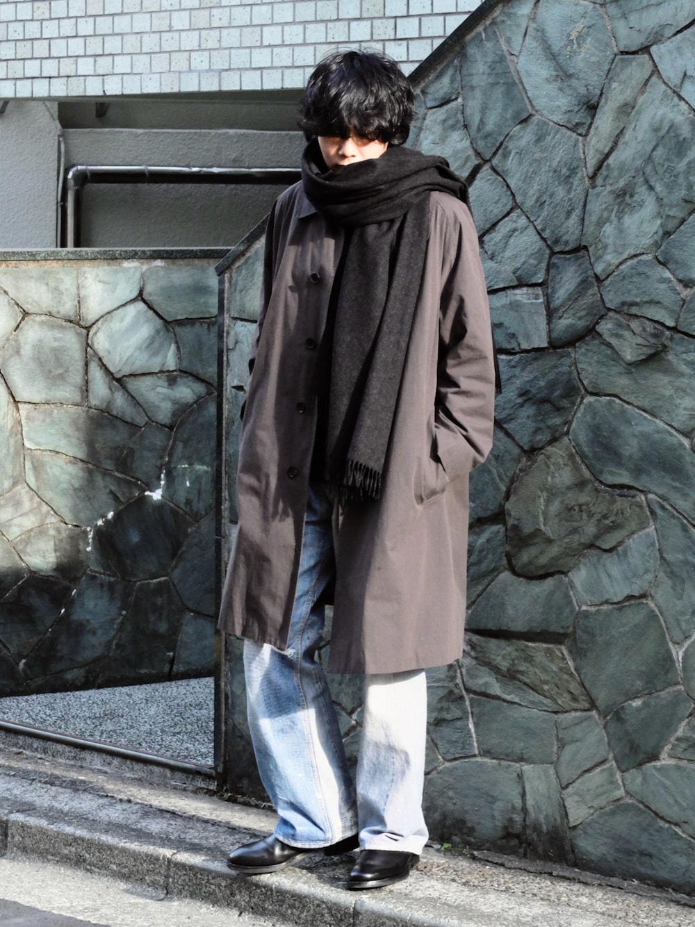 ブルー系のデニムパンツ、ブラック系のブーツ、グレー系のステンカラーコートを着用したメンズの冬コーディネートの1枚目の写真