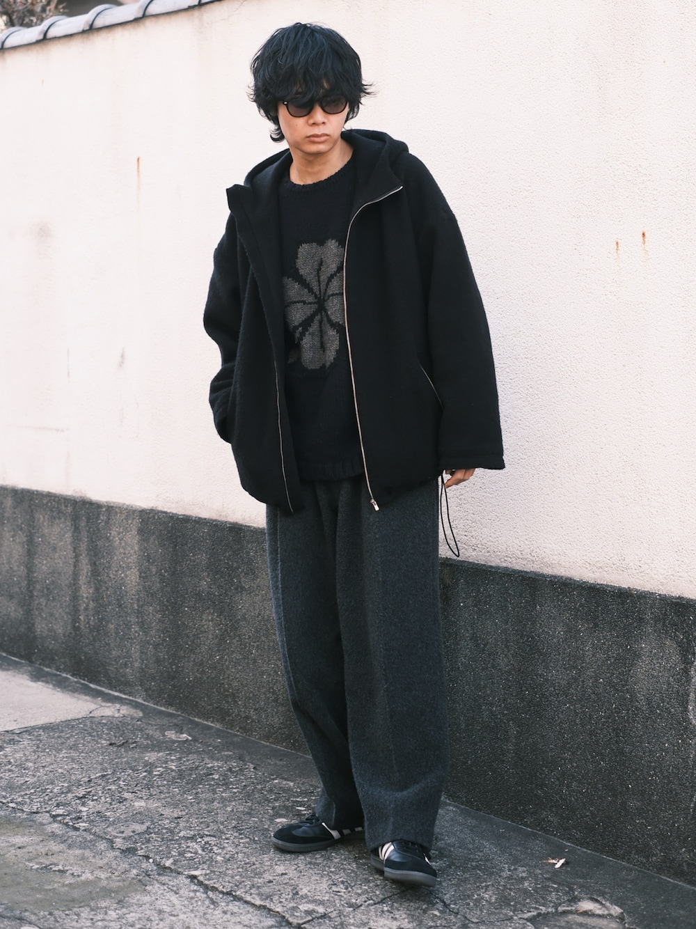 ブラック系のブルゾン、ブルー系のニット/セーター、グレー系のスラックスを着用したメンズの冬コーディネートの1枚目の写真