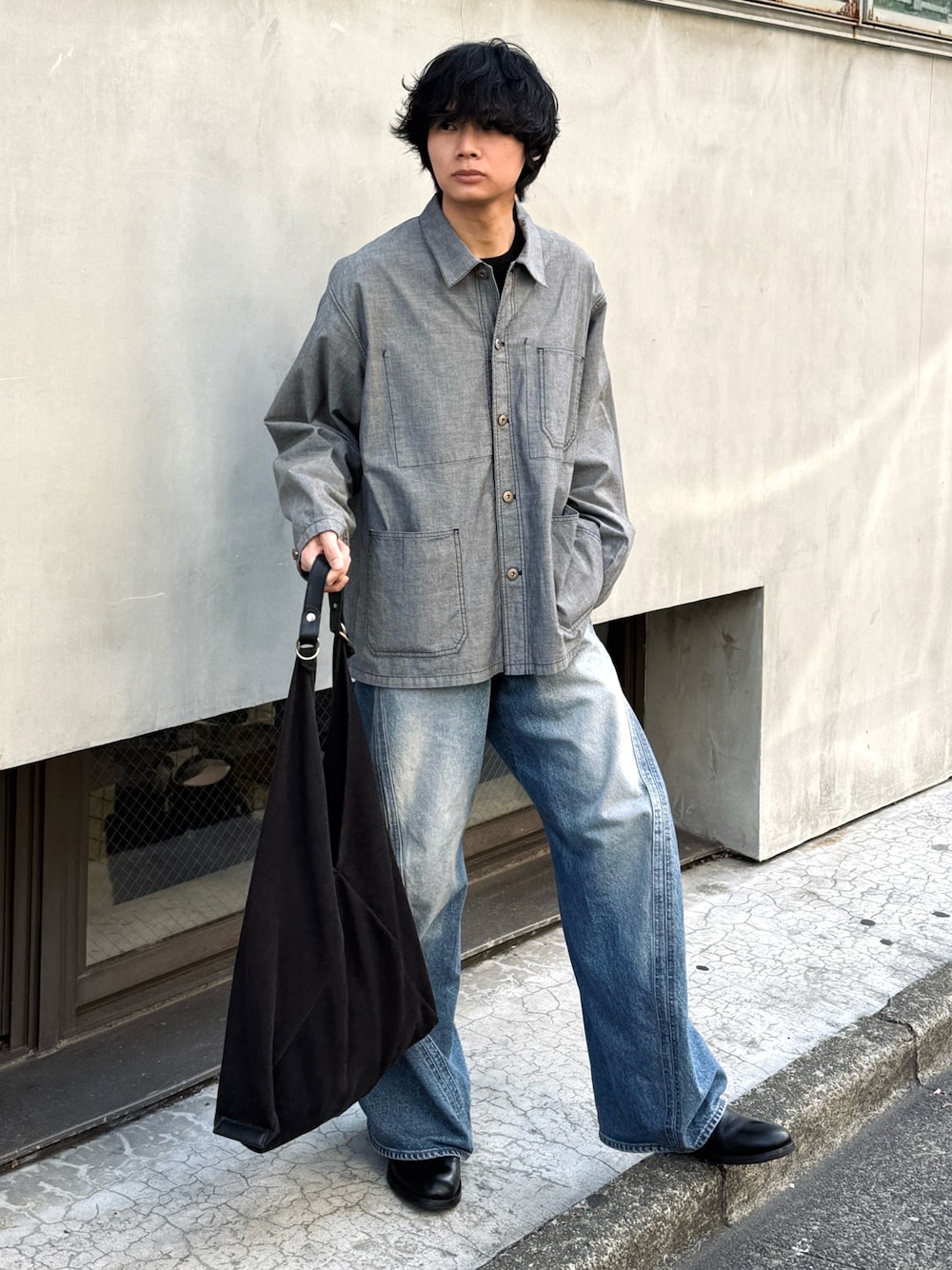 ブラック系のトートバッグ、ブルー系のデニムパンツ、ブラック系のブーツを着用したメンズの春コーディネートの1枚目の写真