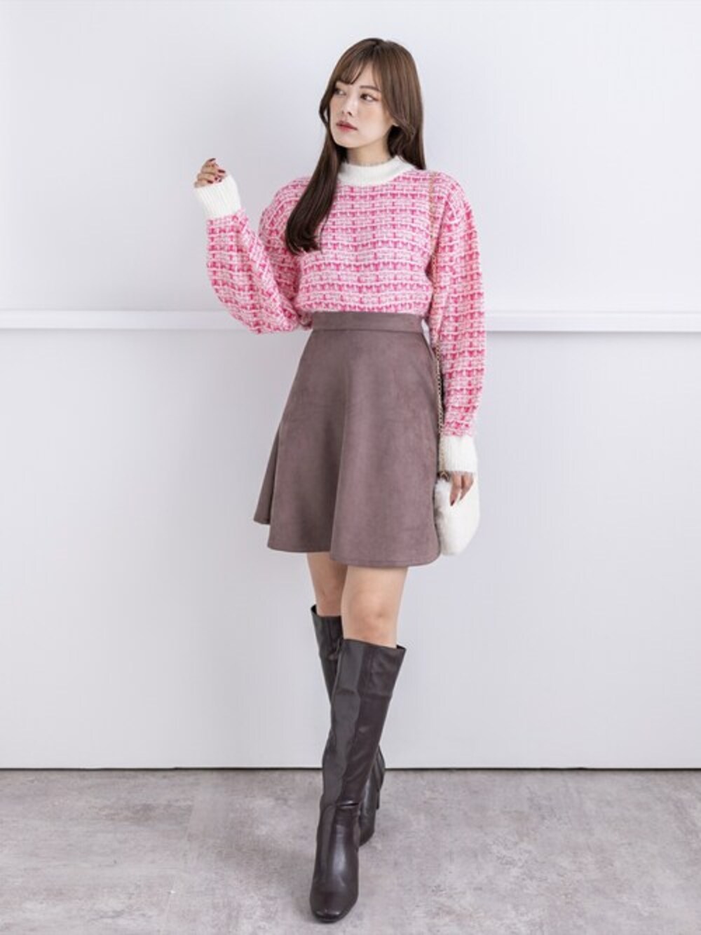 ピンク系のニット/セーター、ブラウン系のスカート、ホワイト系のショルダーバッグを着用したレディースの冬コーディネートの1枚目の写真