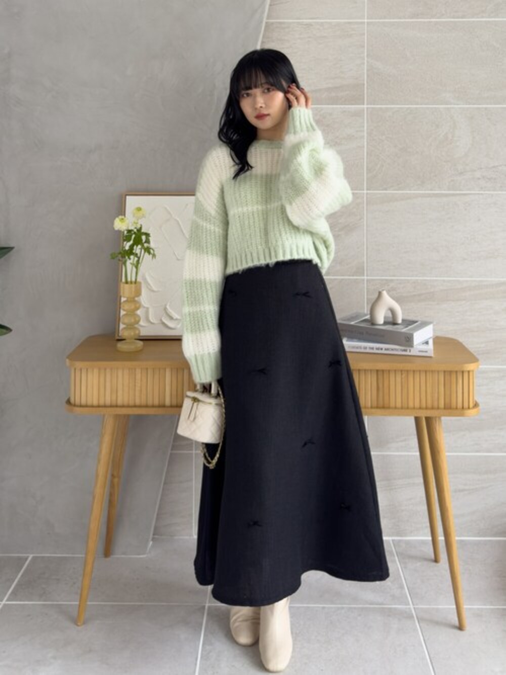 グリーン系のニット/セーター、ブラック系のスカート、ホワイト系のブーツを着用したレディースの冬コーディネートの1枚目の写真
