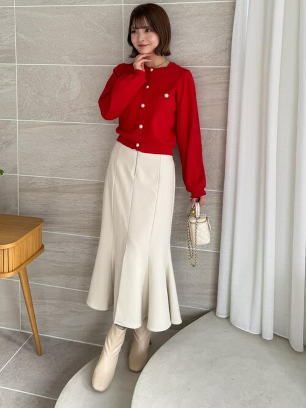 レッド系のカーディガン/ボレロ、ホワイト系のスカート、ホワイト系のブーツを着用したレディースの冬コーディネートの1枚目の写真