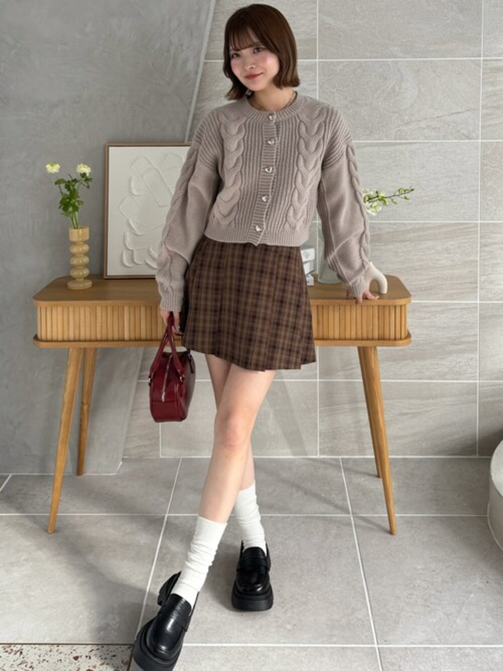 ベージュ系のニット/セーター、ブラウン系のスカート、レッド系のハンドバッグを着用したレディースの冬コーディネートの1枚目の写真