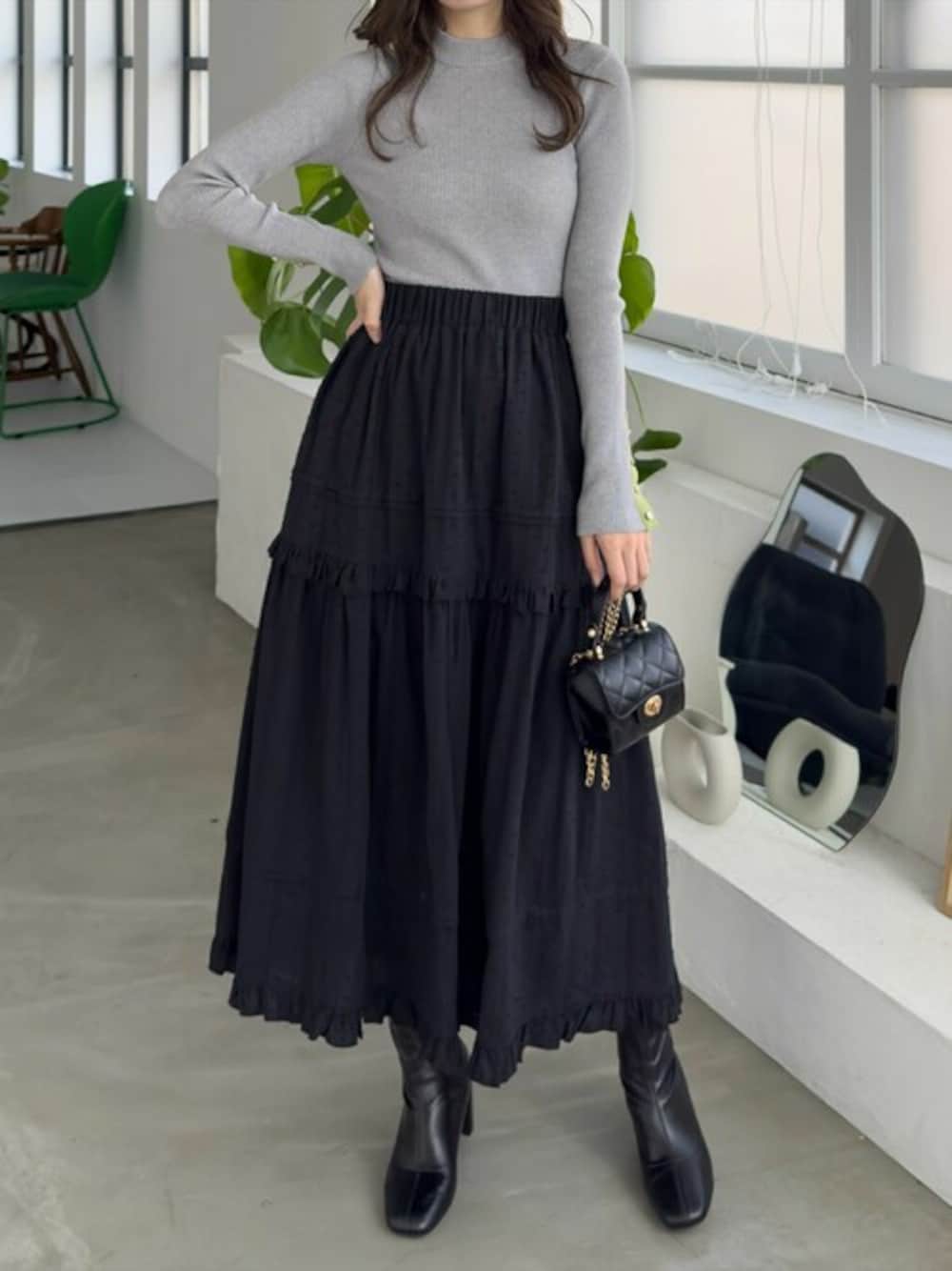 グレー系のニット/セーター、ブラック系のスカート、ブラック系のブーツを着用したレディースの春コーディネートの1枚目の写真