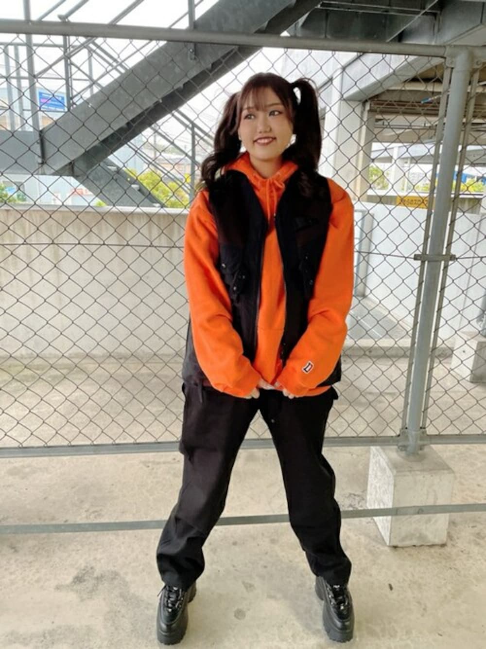 オレンジ系のパーカー、ブラック系のベスト、ブラック系のその他パンツを着用したレディースの冬コーディネートの1枚目の写真