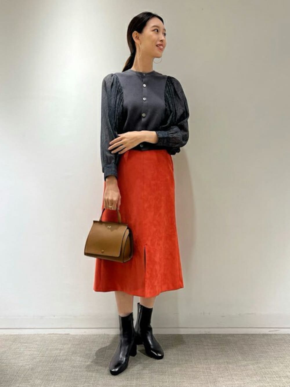 グレー系のニット/セーター、オレンジ系のスカート、イエロー系のハンドバッグを着用したレディースの秋コーディネートの1枚目の写真