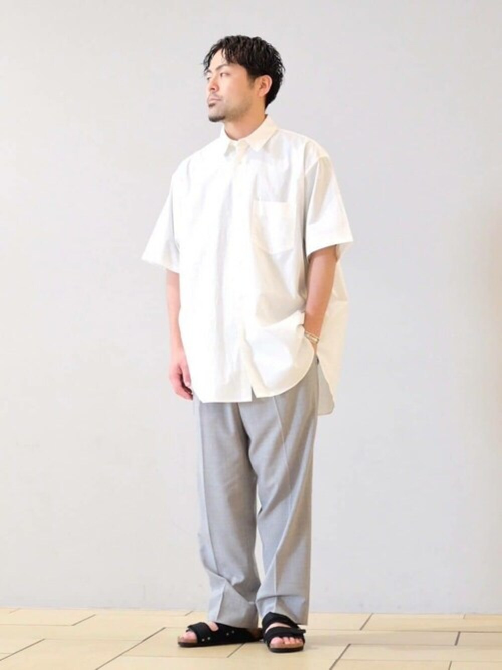 グレー系のスラックス、ホワイト系のシャツ/ブラウス、ブラック系のサンダルを着用したメンズの夏コーディネートの1枚目の写真