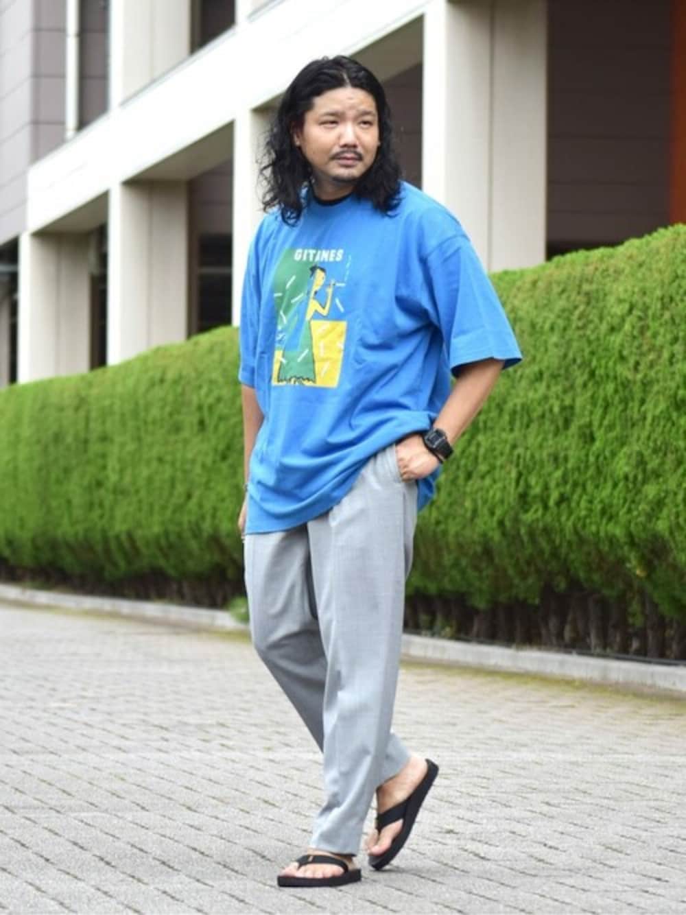ブルー系のTシャツ/カットソー、グレー系のスラックス、ブラック系のサンダルを着用したメンズの夏コーディネートの1枚目の写真