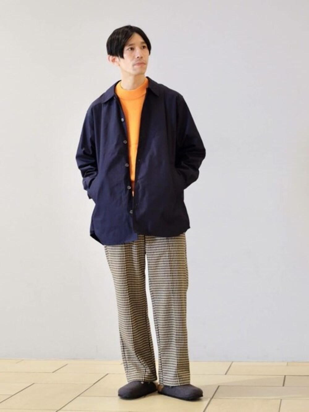 オレンジ系のニット/セーター、ブルー系のシャツ/ブラウス、ベージュ系のスラックスを着用したメンズの秋コーディネートの1枚目の写真