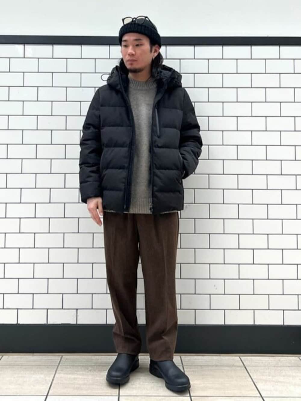 ブラック系のダウンジャケット/コート、ベージュ系のニット/セーター、ブラウン系のスラックスを着用したメンズの冬コーディネートの1枚目の写真