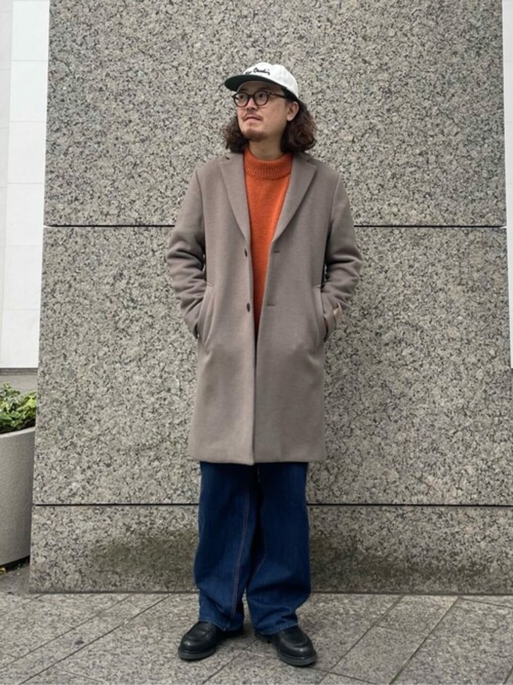 グレー系のチェスターコート、レッド系のニット/セーター、ブルー系のデニムパンツを着用したメンズの冬コーディネートの1枚目の写真