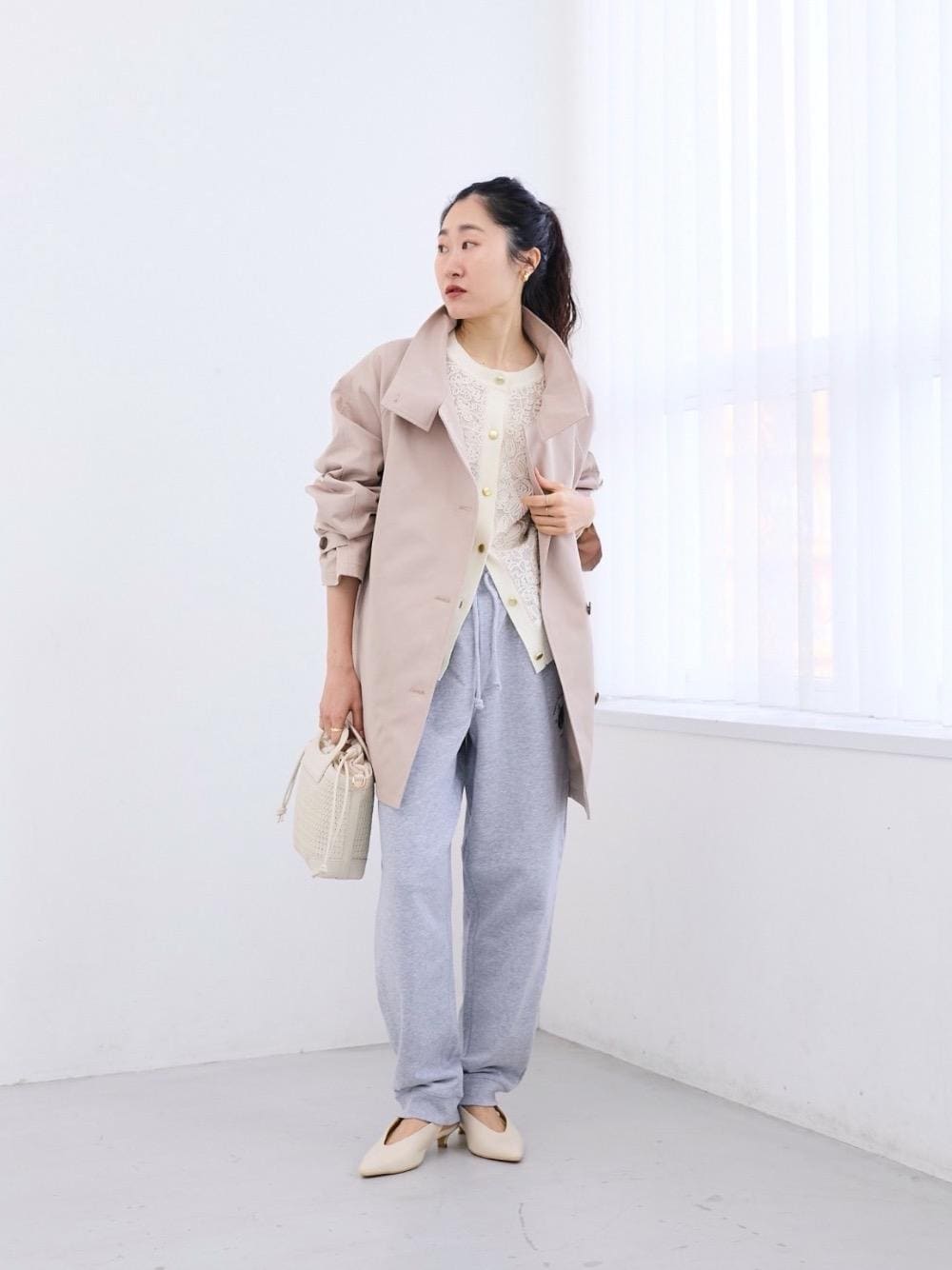 ベージュ系のステンカラーコート、ホワイト系のトートバッグ、ベージュ系のパンプスを着用したレディースの冬コーディネートの1枚目の写真