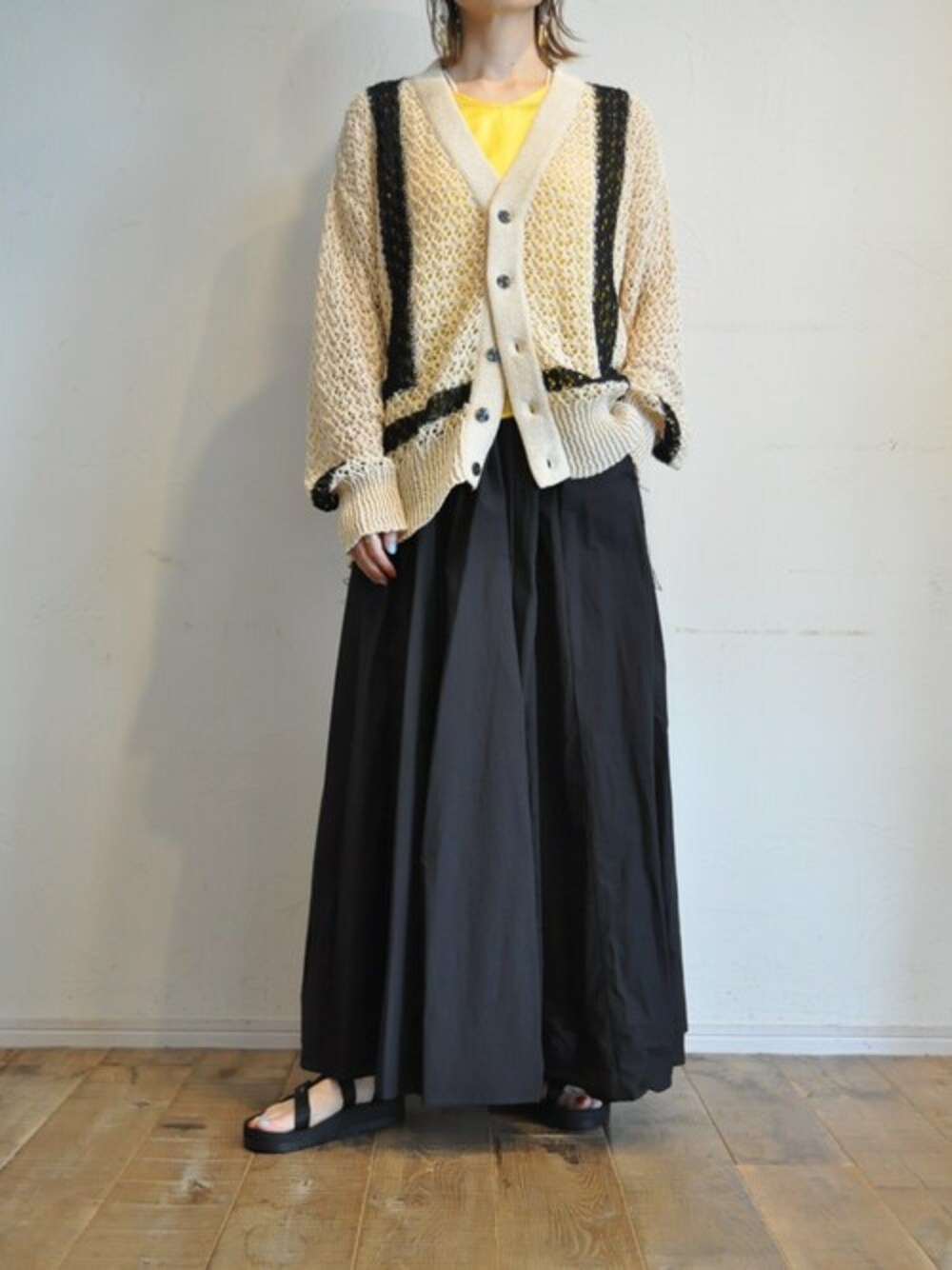 ベージュ系のカーディガン/ボレロ、イエロー系のタンクトップ、ブラック系のスカートを着用したレディースの春コーディネートの1枚目の写真