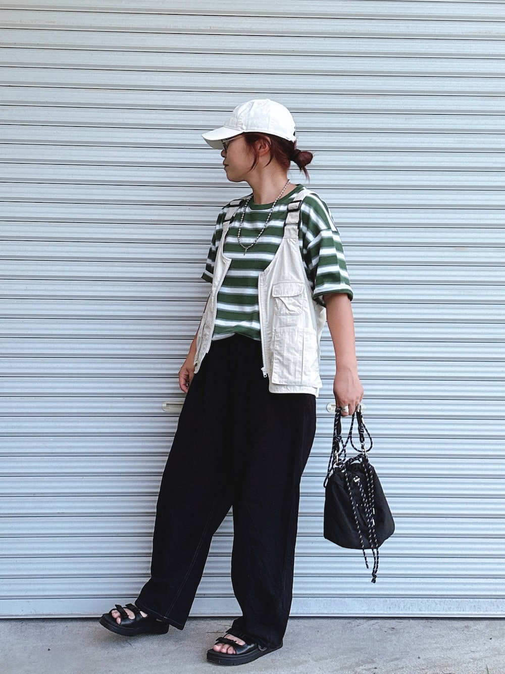 ベージュ系のベスト、グリーン系のTシャツ/カットソー、ブラック系のショルダーバッグを着用したレディースの夏コーディネートの1枚目の写真