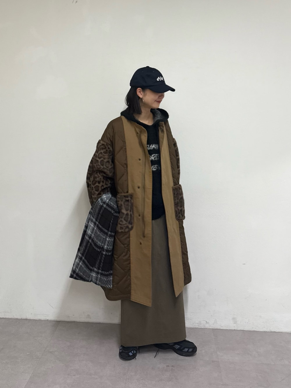 ブラウン系のノーカラーコート、グリーン系のスカート、ブラック系のパーカーを着用したレディースの秋コーディネートの1枚目の写真