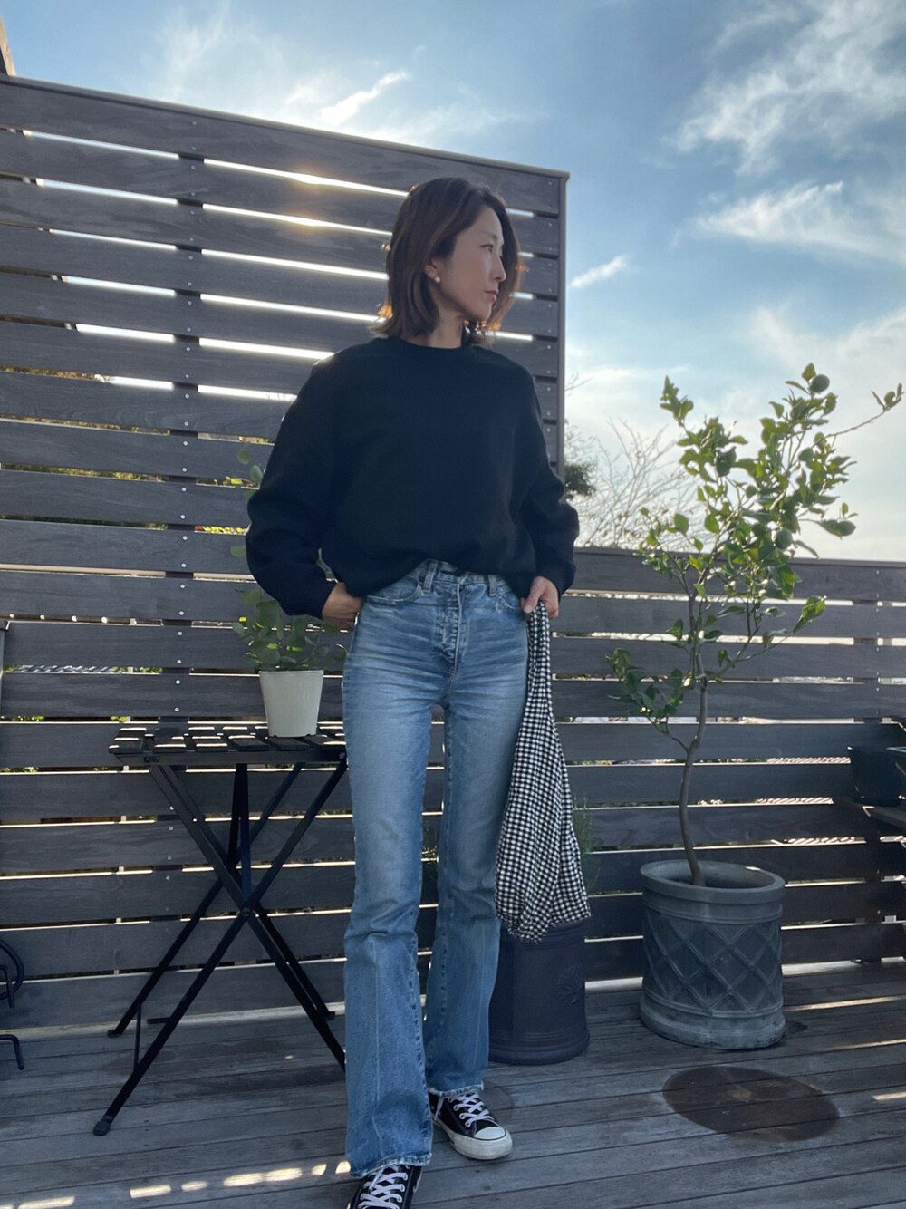 ブルー系のデニムパンツ、ブラック系のスニーカー、ブラック系のショルダーバッグを着用したレディースの秋コーディネートの1枚目の写真