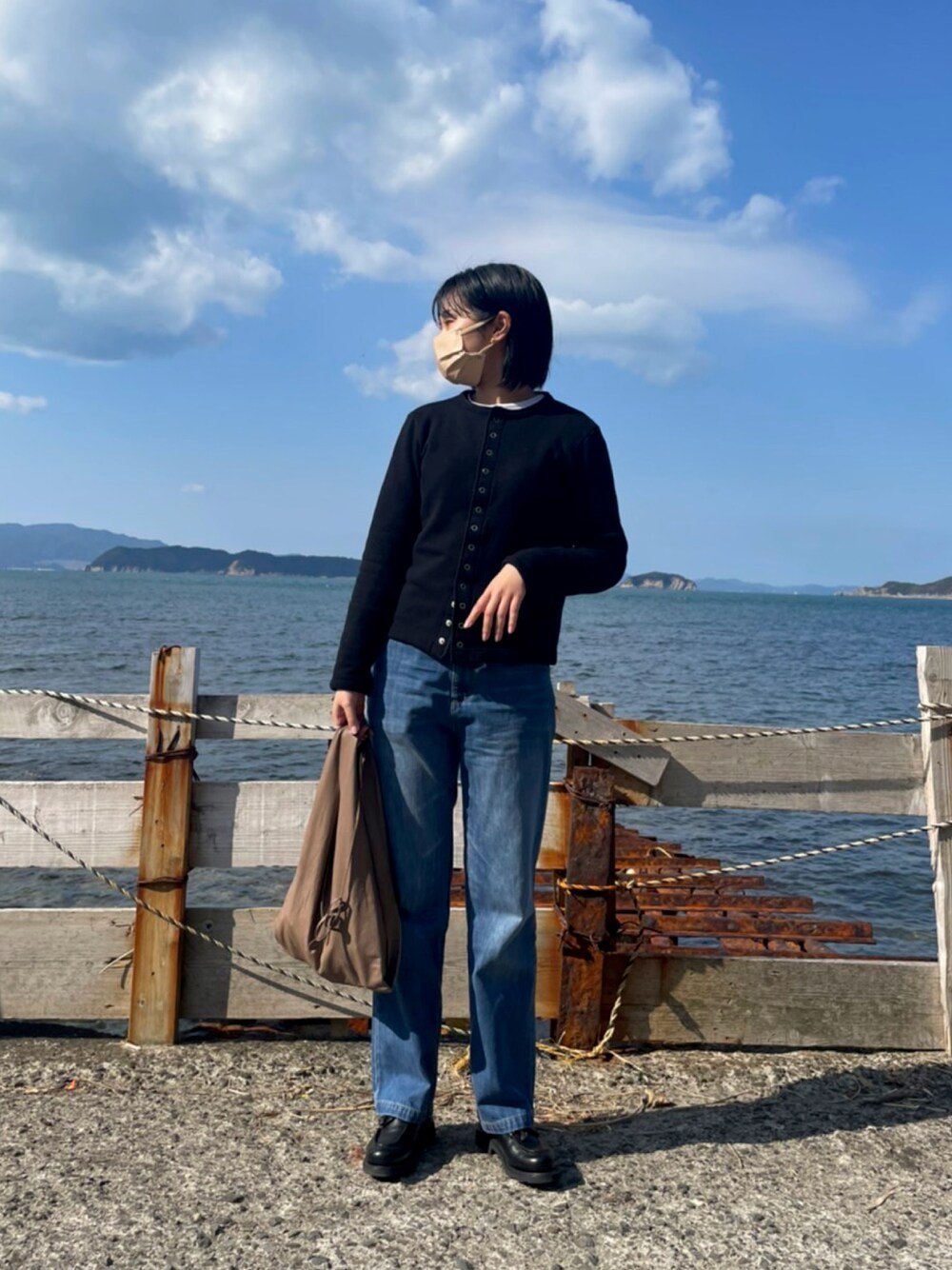 ブラック系のカーディガン/ボレロ、ブルー系のデニムパンツ、ブラウン系のハンドバッグを着用したレディースの冬コーディネートの1枚目の写真