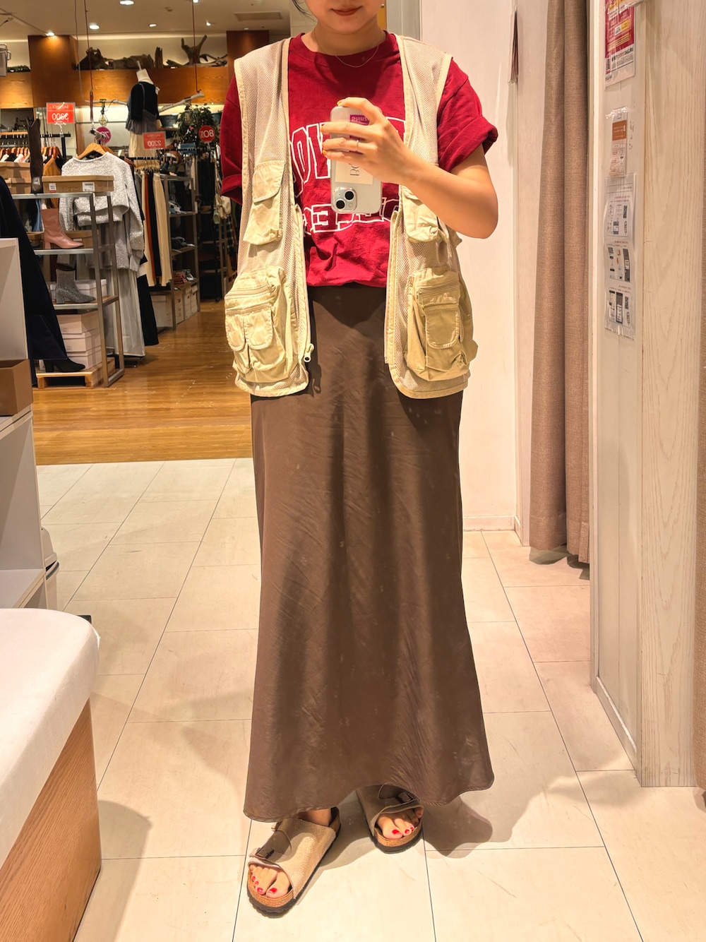 ベージュ系のベスト、ブラウン系のスカート、ベージュ系のサンダルを着用したレディースの秋コーディネートの1枚目の写真