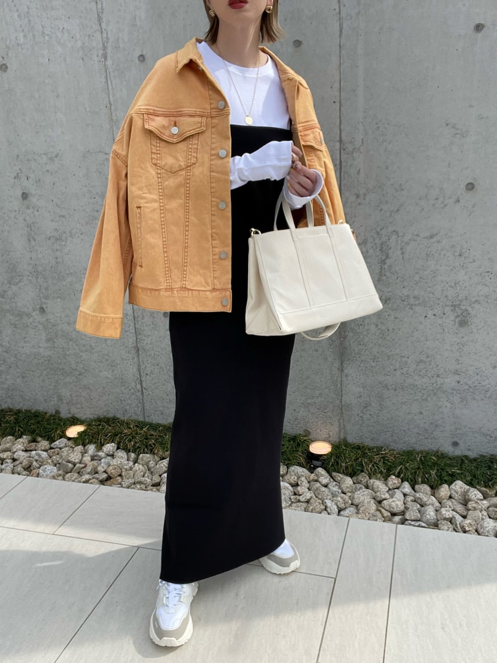 ホワイト系のトートバッグ、オレンジ系のデニムジャケット、ブラック系のワンピースを着用したレディースの春コーディネートの1枚目の写真