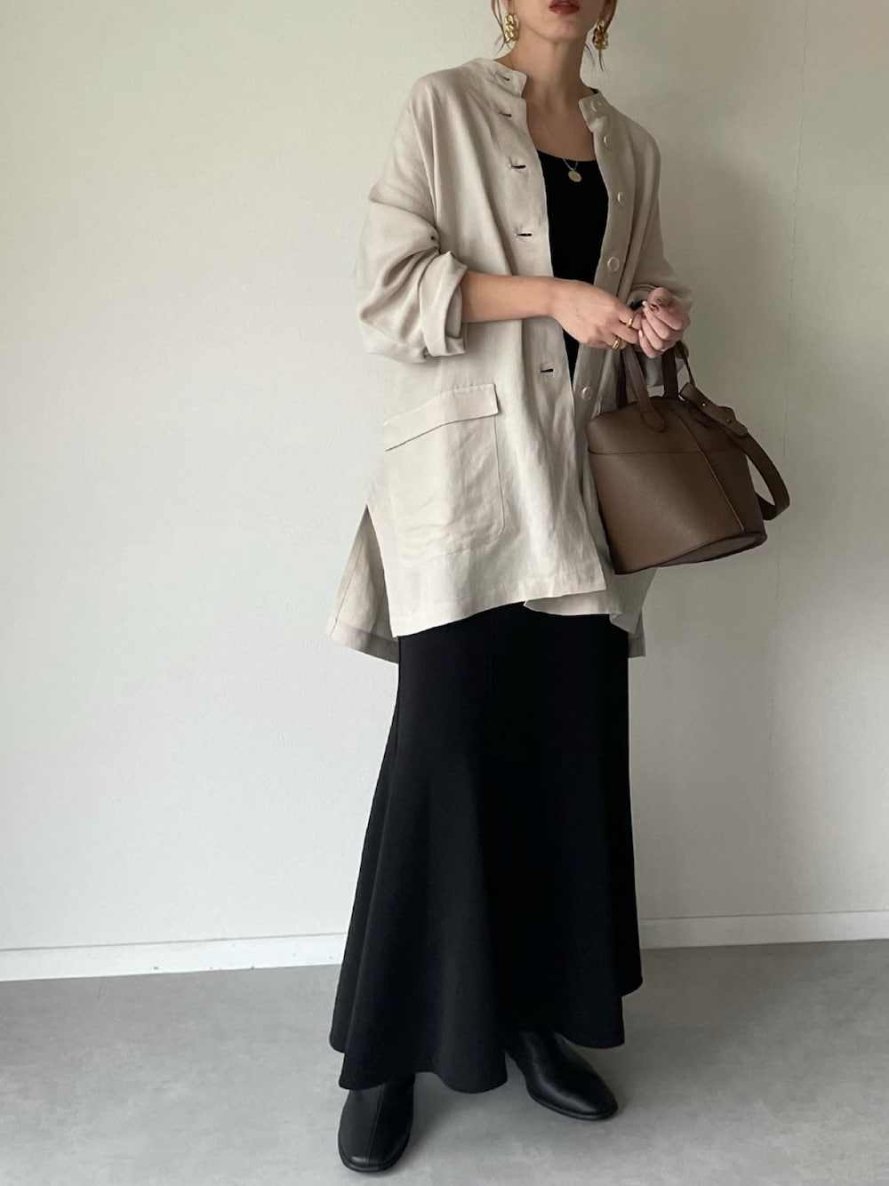 ベージュ系のその他アウター、ブラック系のスカート、ブラウン系のショルダーバッグを着用したレディースの冬コーディネートの1枚目の写真