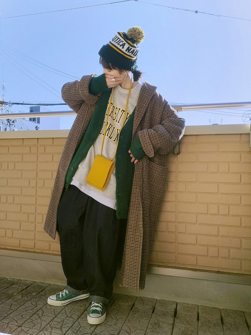 ベージュ系のチェスターコート、グリーン系のカーディガン/ボレロ、ブルー系のデニムパンツを着用したレディースの秋コーディネートの1枚目の写真