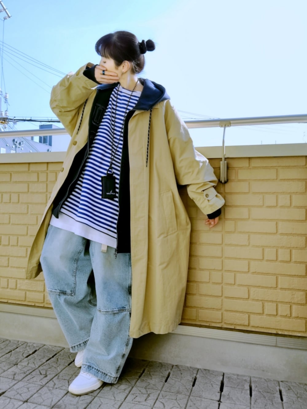 ホワイト系のスニーカー、ブルー系のデニムパンツ、ベージュ系のステンカラーコートを着用したレディースの春コーディネートの1枚目の写真