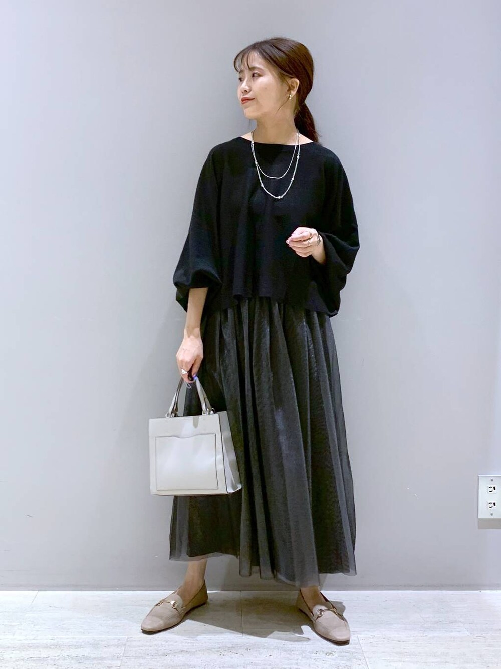 ブラック系のニット/セーター、ベージュ系のローファー、ベージュ系のショルダーバッグを着用したレディースの秋コーディネートの1枚目の写真