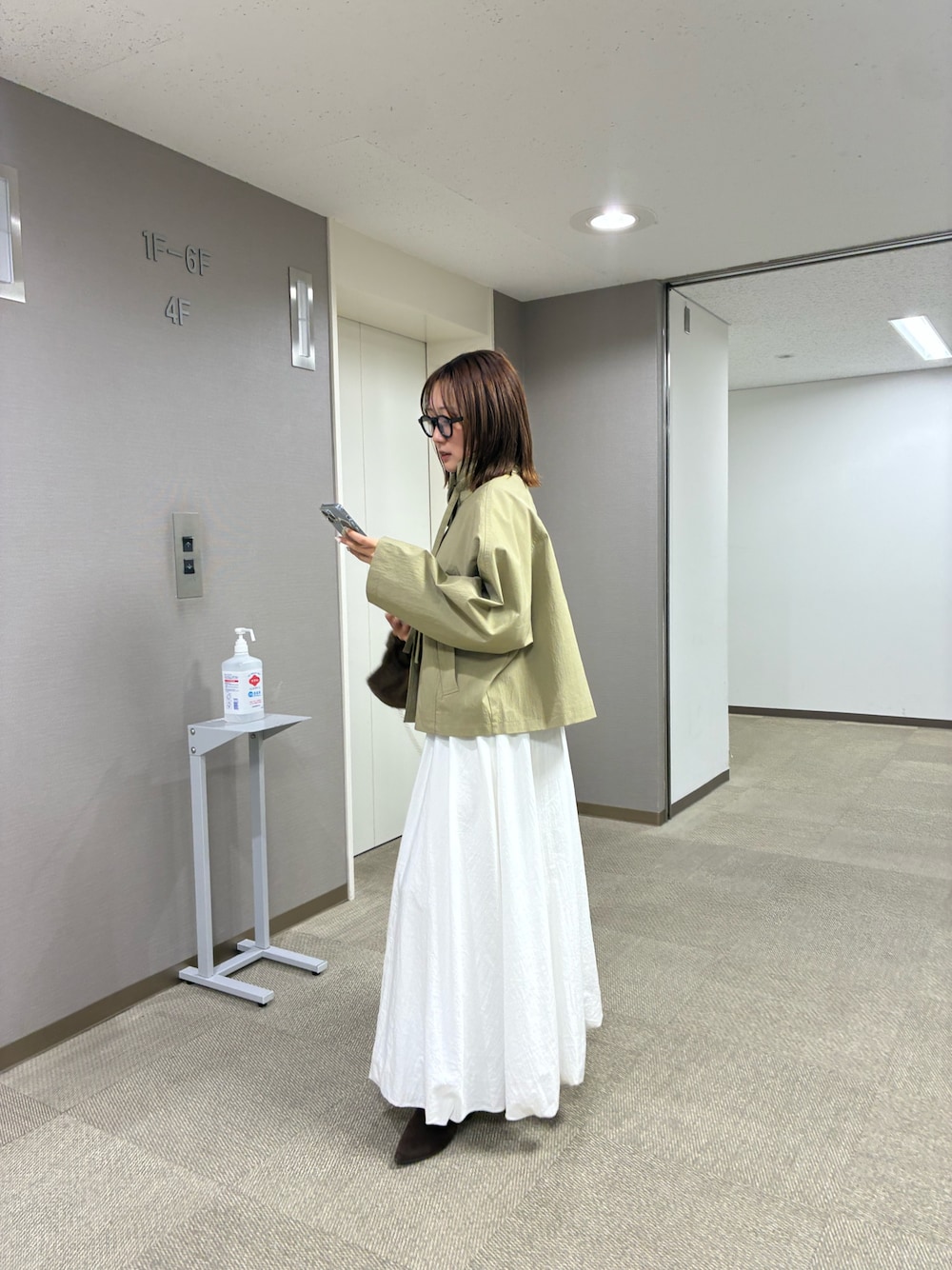 ベージュ系のトレンチコート、ホワイト系のスカートを着用したレディースの冬コーディネートの1枚目の写真