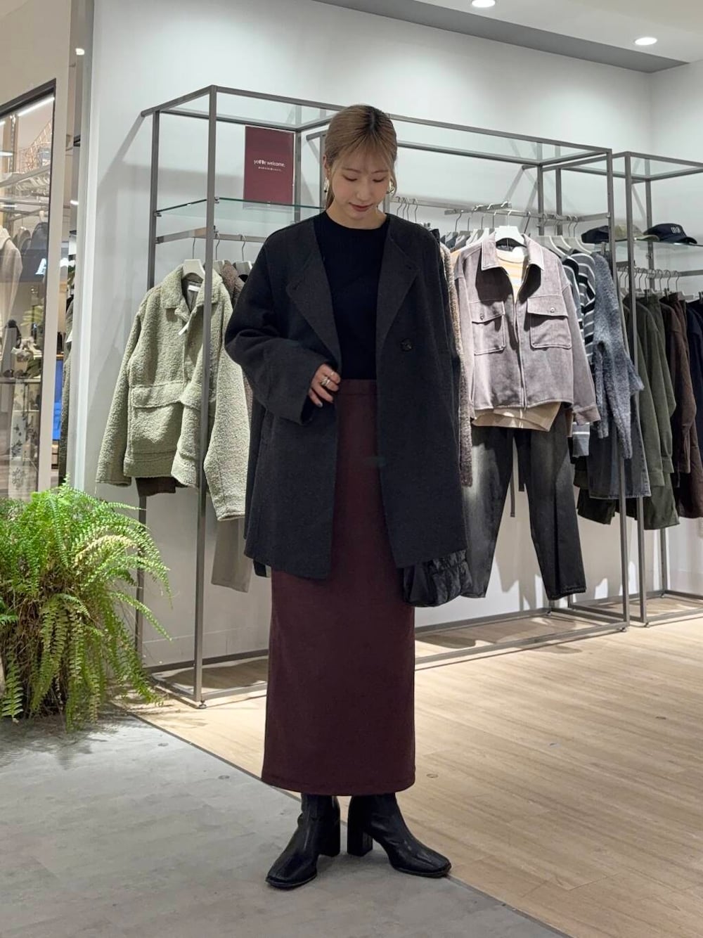 グレー系のノーカラーコート、ブラック系のブーツ、ブラック系のニット/セーターを着用したレディースの冬コーディネートの1枚目の写真