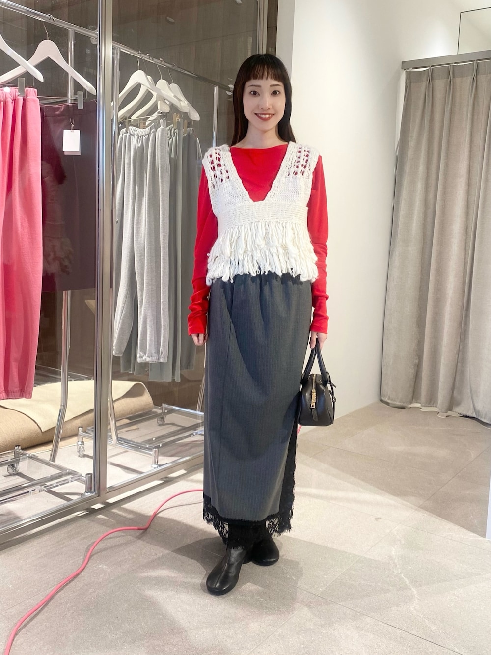 グレー系のスカート、レッド系のTシャツ/カットソー、ホワイト系のベストを着用したレディースの夏コーディネートの1枚目の写真